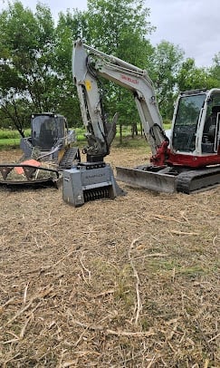 Small excavators and heavy machinery parked on dirt ground with trees in background