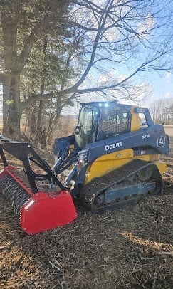 Yellow and blue John Deere compact track loader with red snow plow attachment in winter landscape