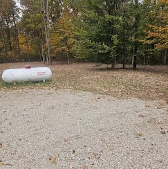Gravel lot with white cylindrical tank and autumn trees in background
